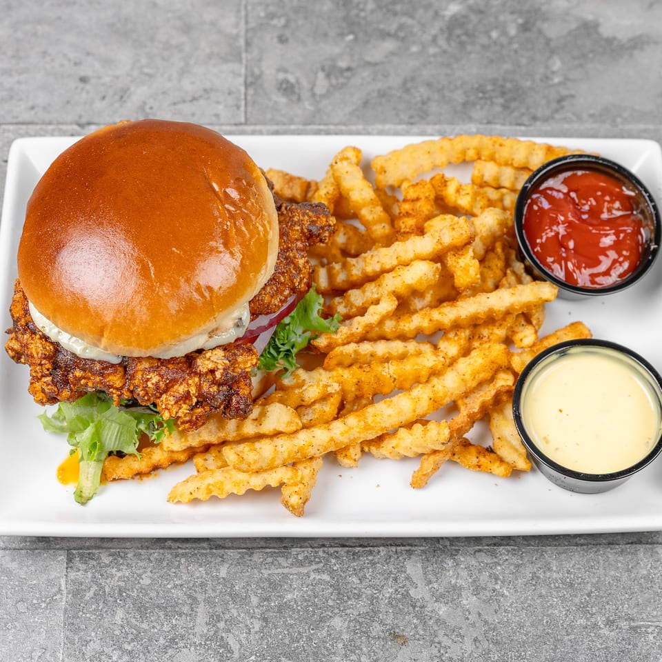 Crispy chicken sandwich with lettuce, tomato, and creamy sauce served with seasoned crinkle-cut fries, ketchup, and cheese sauce.