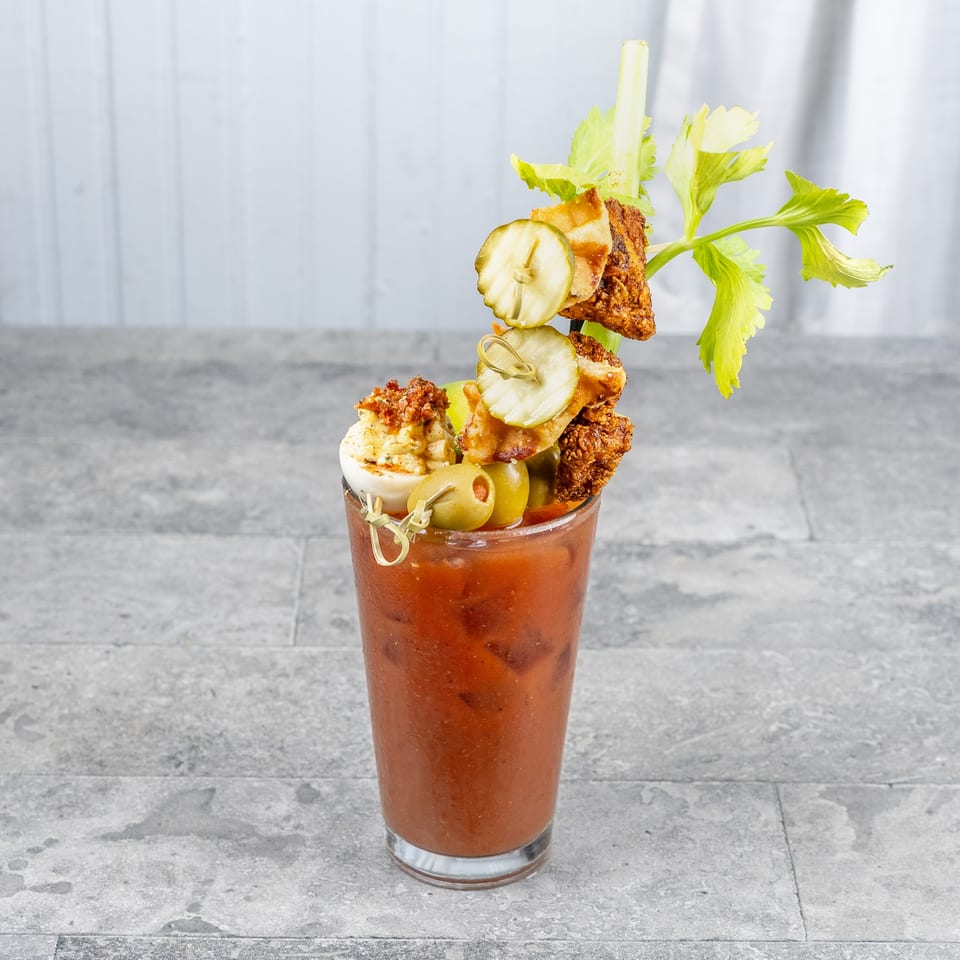 Bloody Mary cocktail garnished with fried chicken, pickles, olives, deviled egg, celery, and crispy toppings.