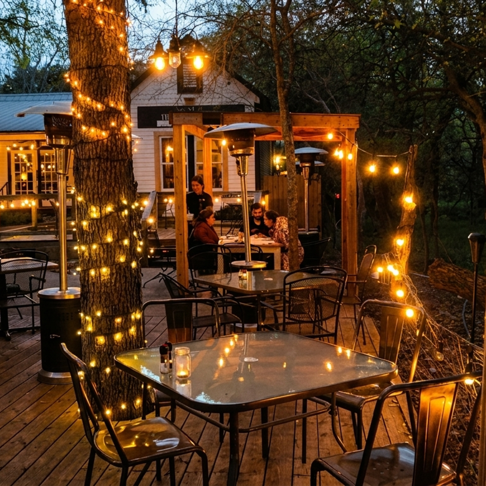 An outdoor restaurant patio at dusk, illuminated by string lights wrapped around trees and railings.