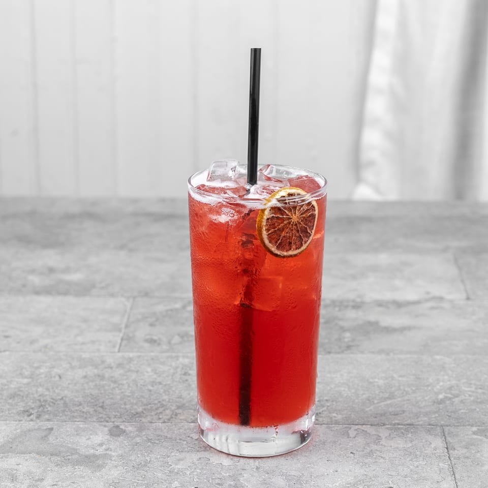 Red iced cocktail with a black straw and dried citrus garnish in a clear glass on a stone tabletop.