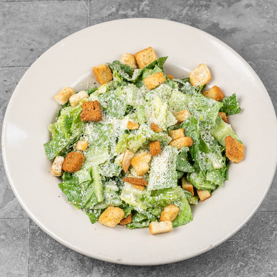 Caesar salad with crisp romaine lettuce, golden croutons, creamy dressing, and grated Parmesan on a white plate.